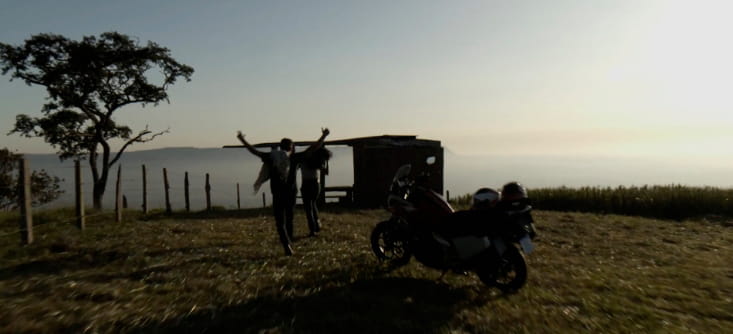 Foto do horizonte no alto de uma montanha com uma moto e duas pessoas observando o céu.